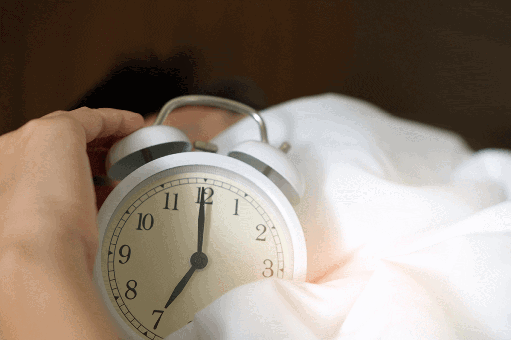 person in bed holding a white alarm clock