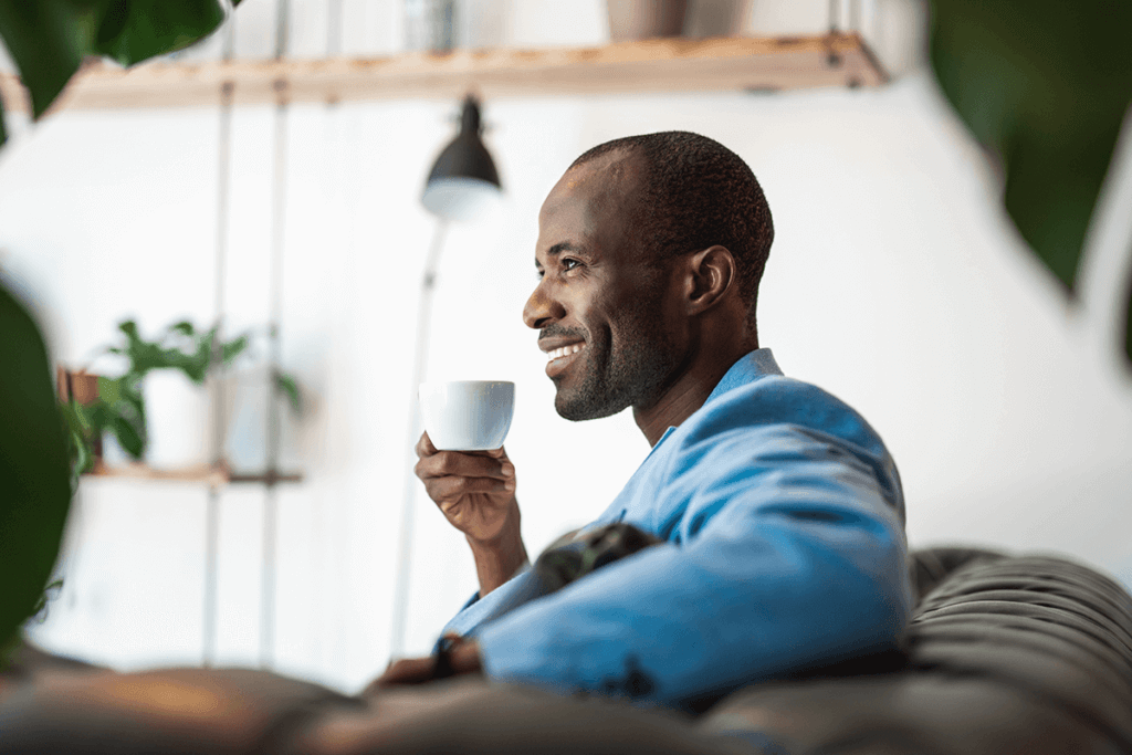 man sitting on couch smiling and drinking from white cup