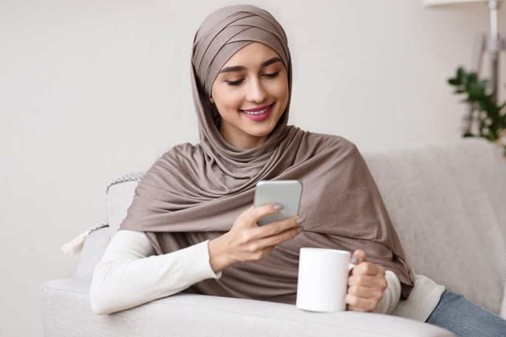 woman sitting holding a white mug looking at her phone in her living room