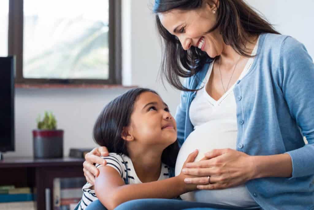 pregnant woman looking down at her child and holding her near her belly