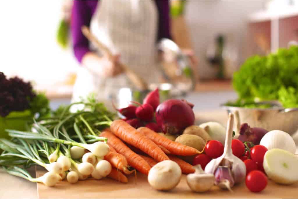 A young woman cooking in a kitchen with an assortment of colorful vegetables.