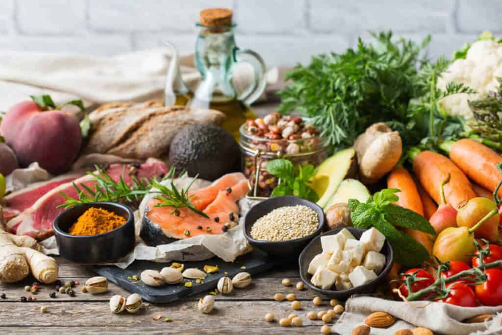 Variety of healthy protein, vegetables, fruit, herbs, grains, oil, and nuts on a kitchen counter.