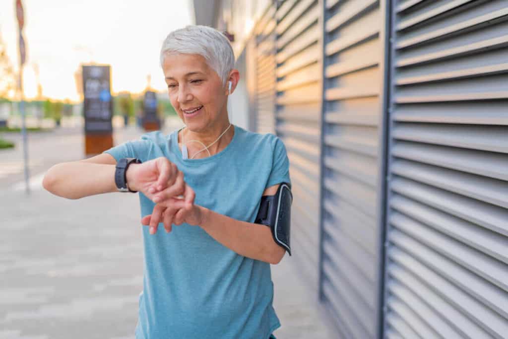 woman looking at her smart watch as she is beginning to run outside