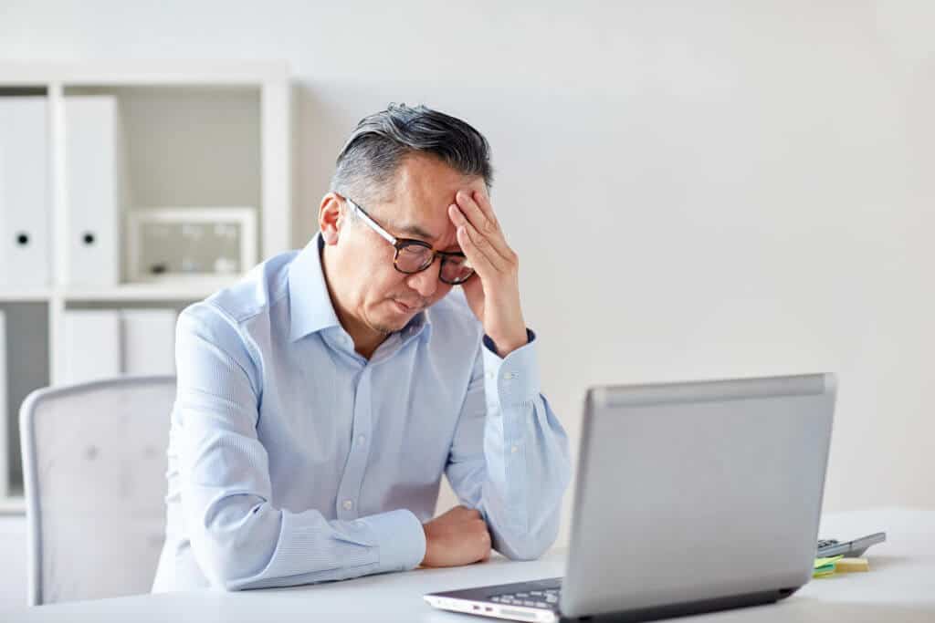 male with a hand on his head in front of a laptop