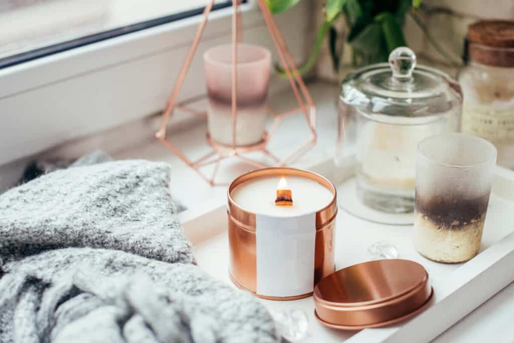 candle lit on a white holder with accessories surrounding it next to window