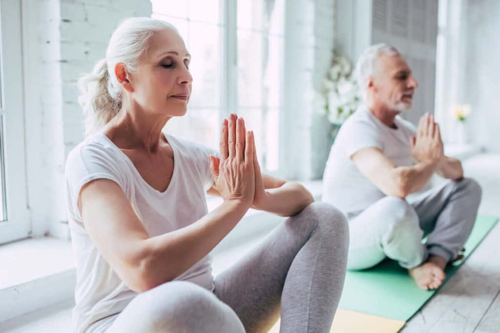 elder couple meditating together on yoga mats