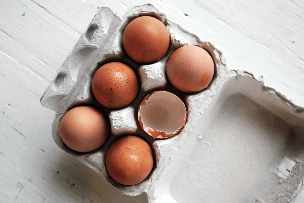 six brown eggs in white carton, one egg is broken