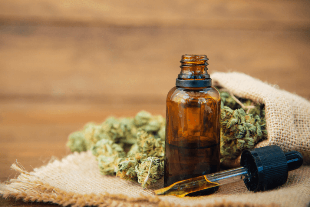 Dried cannabis plant and oil dropper on a wood table.