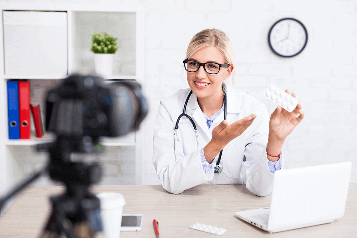 practitioner sitting at desk, holding up supplements and looking into a camera