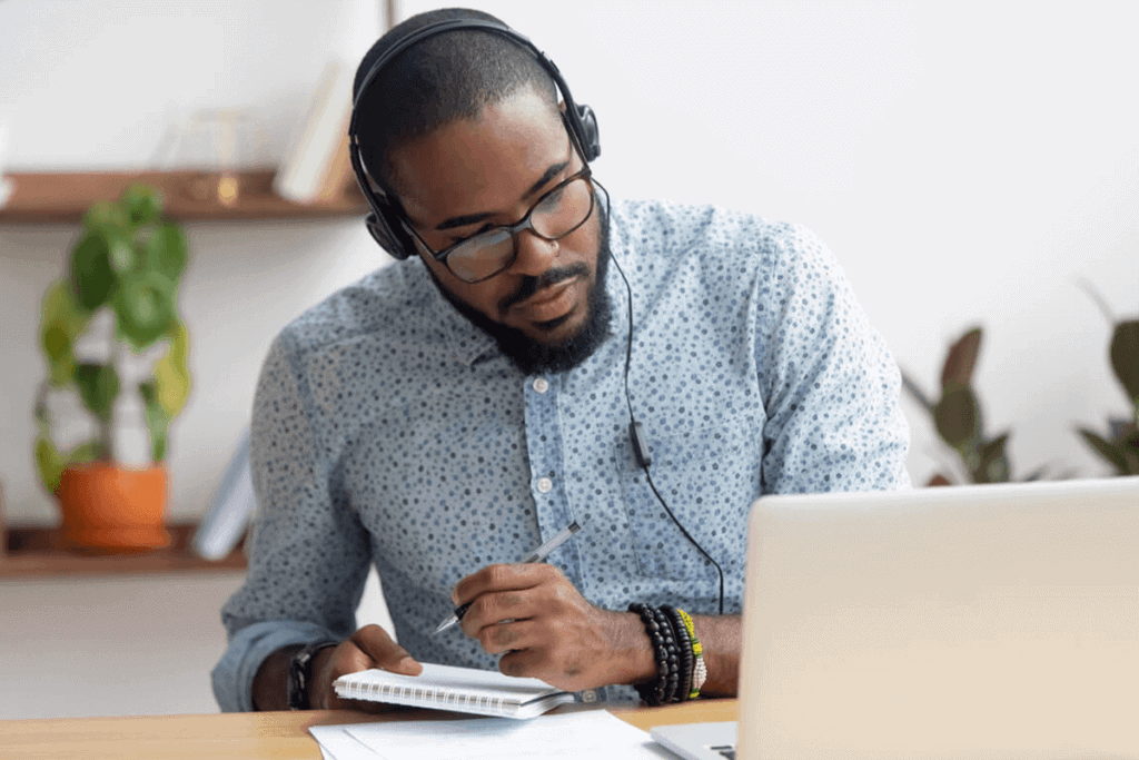 person with headphones taking notes and looking at their computer