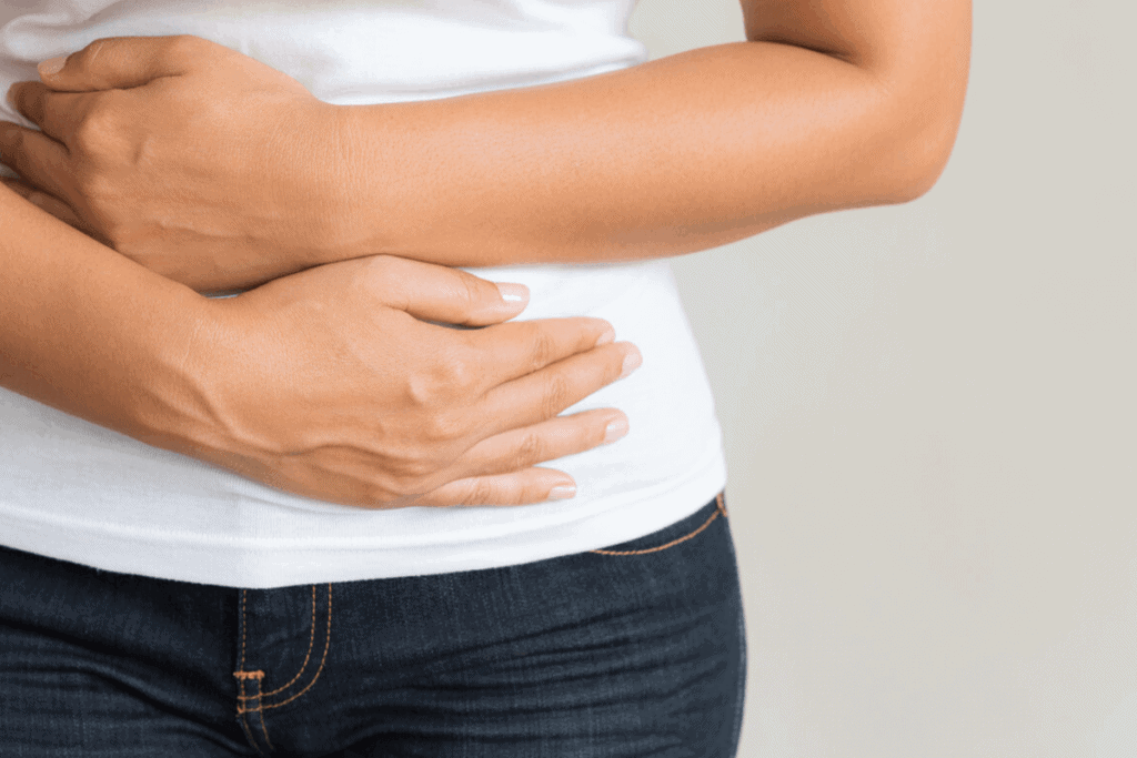 Woman in white t-shirt holding her stomach in pain.